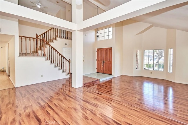 entryway featuring light wood finished floors, baseboards, ceiling fan, stairs, and high vaulted ceiling