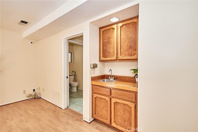 interior space with visible vents, light wood finished floors, a sink, light countertops, and brown cabinets