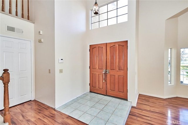 foyer featuring visible vents, light wood-style flooring, and a towering ceiling