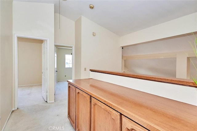 corridor with light carpet, baseboards, and vaulted ceiling