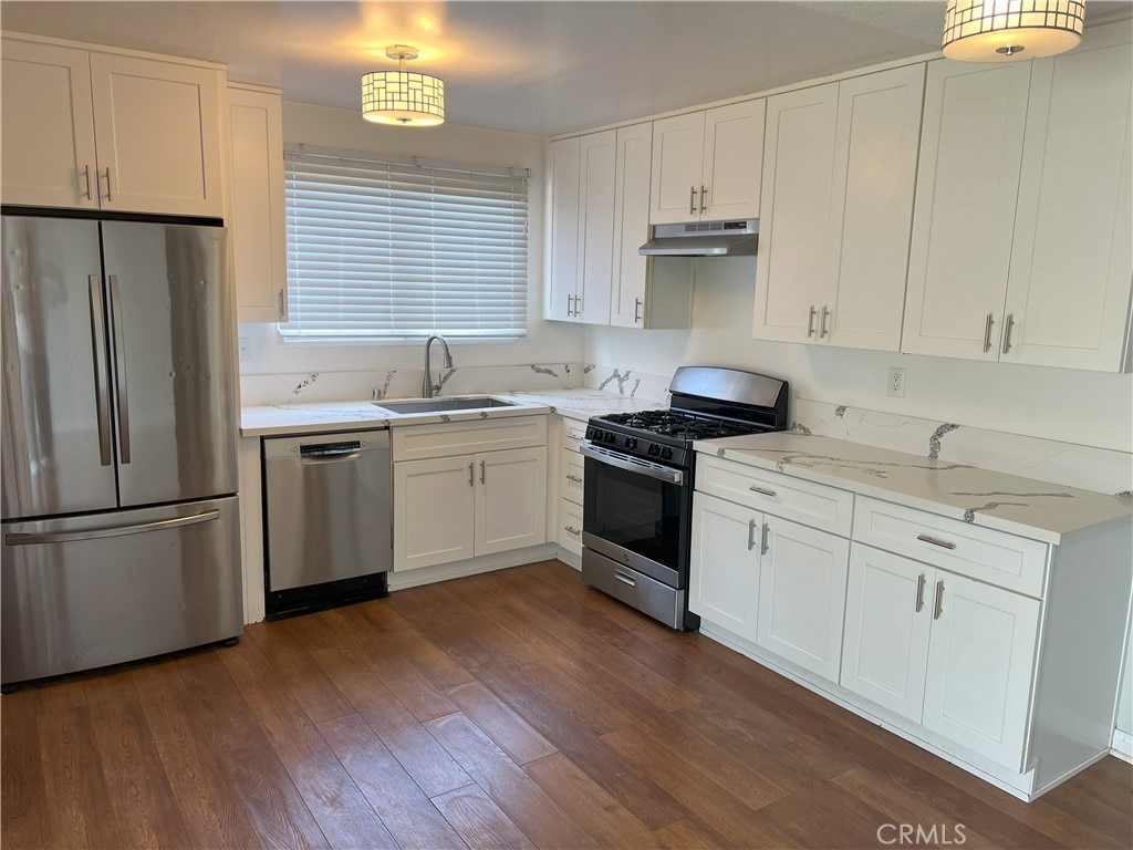 kitchen featuring a sink, under cabinet range hood, dark wood-style floors, white cabinetry, and stainless steel appliances