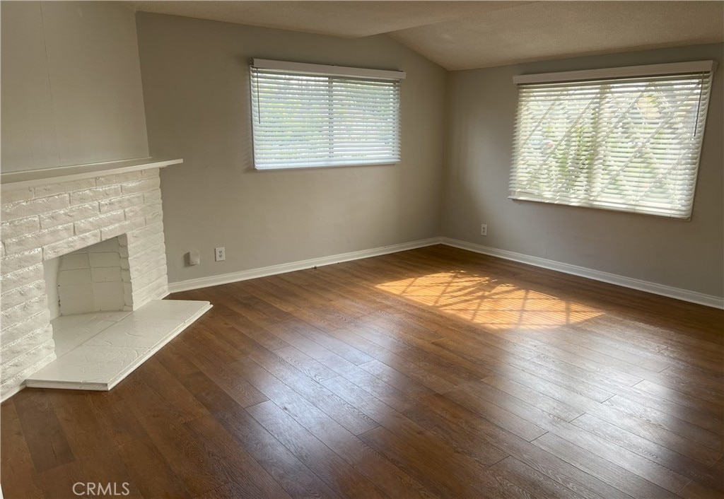 unfurnished living room featuring baseboards, a brick fireplace, and hardwood / wood-style flooring