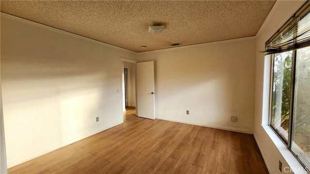 empty room featuring visible vents, a textured ceiling, wood finished floors, crown molding, and baseboards