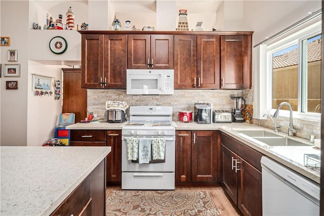 kitchen with white appliances, light stone counters, a sink, light wood-style floors, and tasteful backsplash