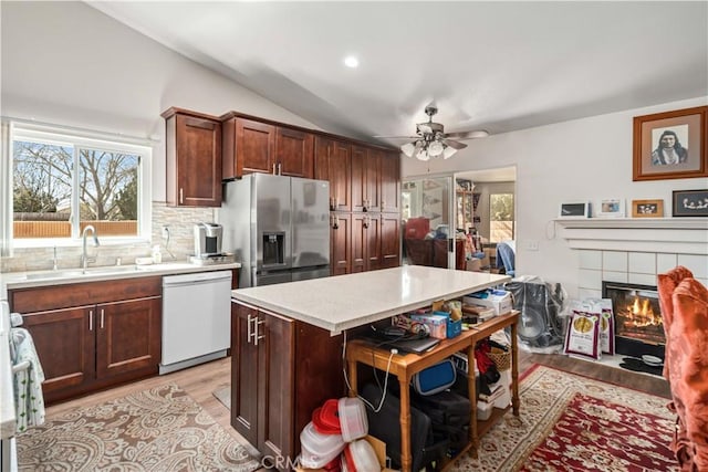 kitchen with decorative backsplash, a tile fireplace, white dishwasher, stainless steel fridge, and a sink