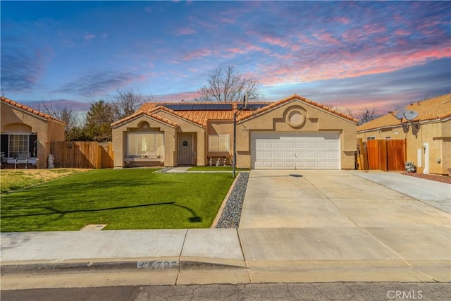 mediterranean / spanish-style home with solar panels, fence, stucco siding, a yard, and driveway