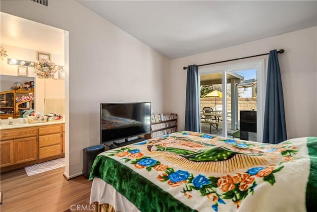 bedroom featuring lofted ceiling, ensuite bath, wood finished floors, and access to outside