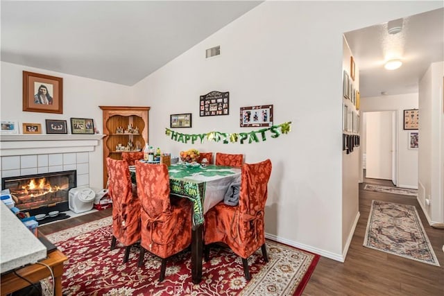 dining area featuring wood finished floors, visible vents, baseboards, lofted ceiling, and a tiled fireplace