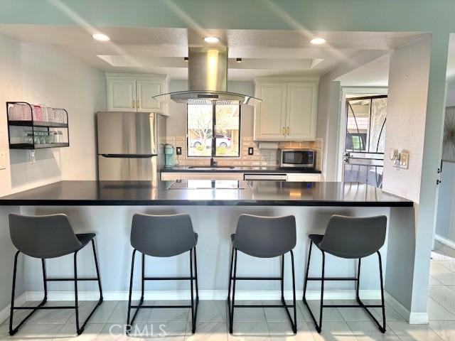 kitchen featuring island exhaust hood, a sink, tasteful backsplash, dark countertops, and stainless steel appliances