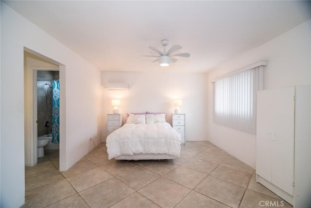 bedroom featuring a wall unit AC, light tile patterned flooring, a ceiling fan, and ensuite bathroom