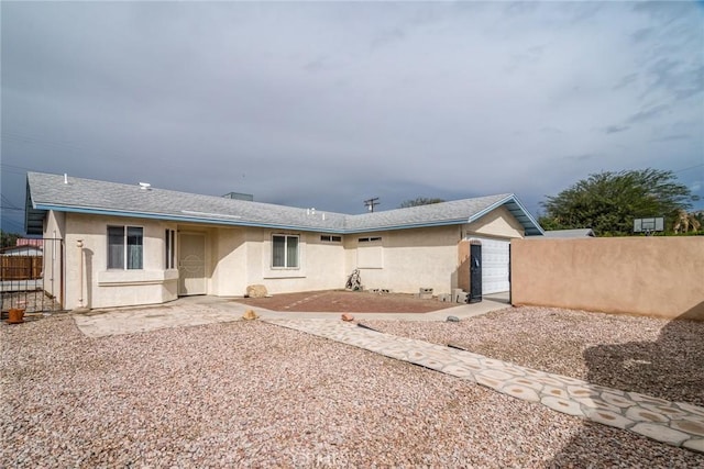 back of property featuring fence, a garage, roof with shingles, and stucco siding