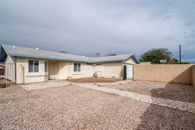 back of property with stucco siding, a shingled roof, and fence