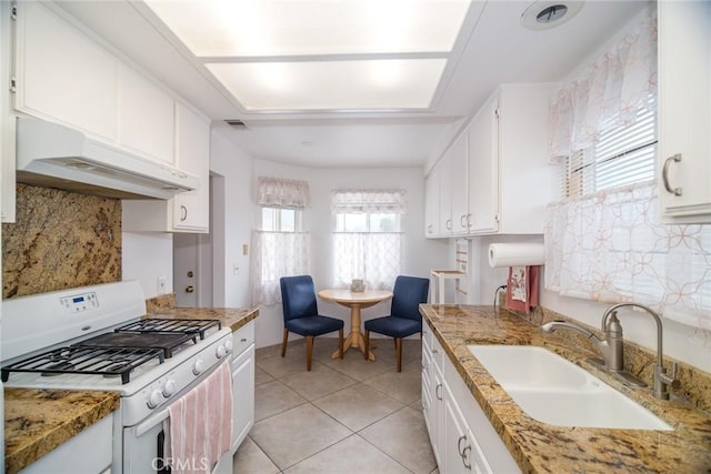 kitchen featuring white range with gas cooktop, under cabinet range hood, a sink, white cabinetry, and light tile patterned floors