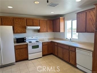 kitchen featuring visible vents, under cabinet range hood, brown cabinetry, white appliances, and a sink