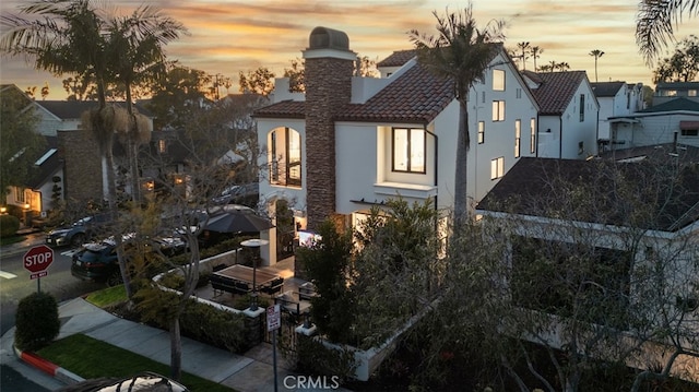 exterior space with a tiled roof, a chimney, and stucco siding