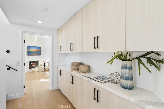 bar with a stone fireplace, recessed lighting, light wood-type flooring, and baseboards