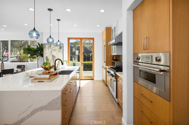 kitchen with modern cabinets, under cabinet range hood, light stone counters, a sink, and stainless steel appliances