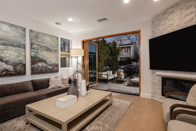 living area with a stone fireplace, recessed lighting, visible vents, and wood-type flooring