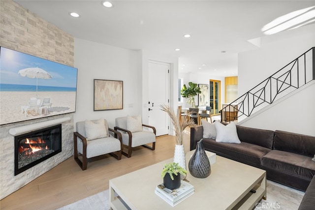 living room with a large fireplace, recessed lighting, stairway, and light wood-type flooring