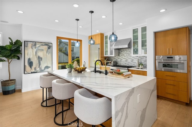 kitchen with brown cabinets, a large island, stainless steel appliances, light wood-style floors, and decorative backsplash