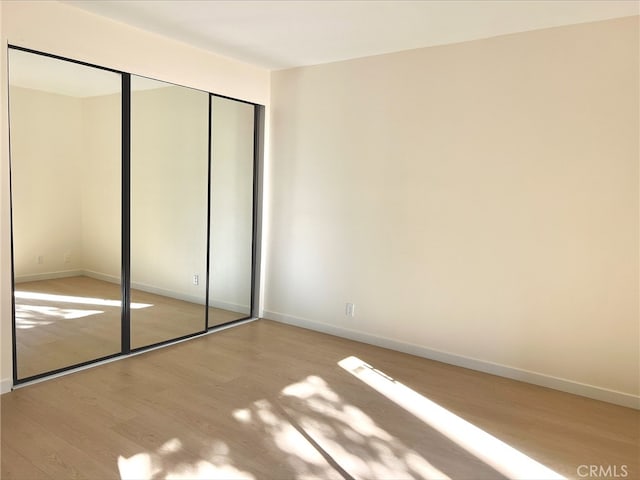 unfurnished bedroom with light wood-style flooring, baseboards, and a closet