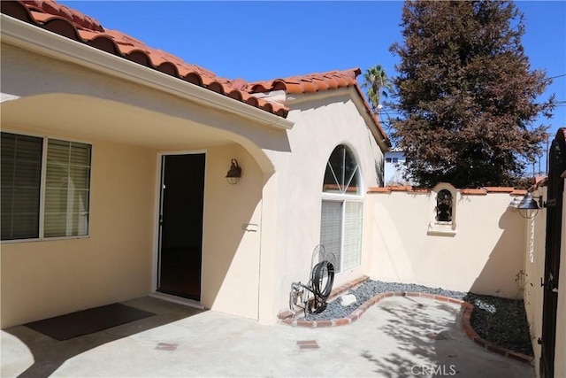 property entrance featuring stucco siding, a tile roof, a patio, and fence