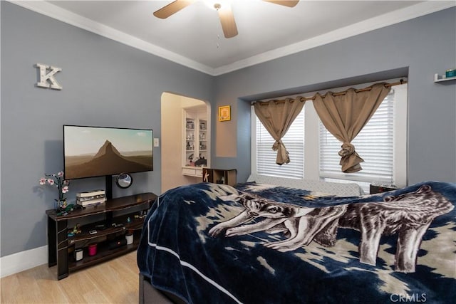 bedroom featuring arched walkways, crown molding, light wood finished floors, baseboards, and ceiling fan