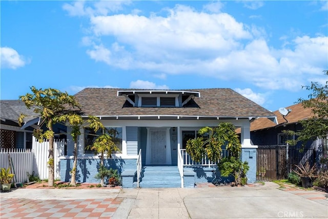 bungalow with a porch, roof with shingles, and fence