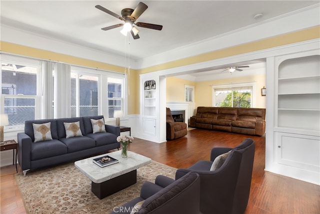 living area featuring built in features, a fireplace, and a ceiling fan