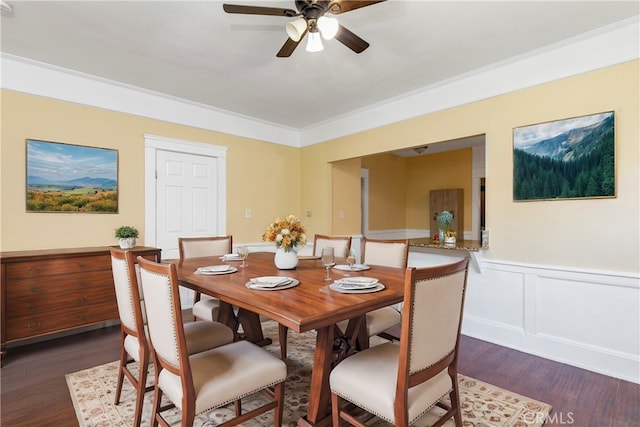 dining space with dark wood-style floors, a ceiling fan, a wainscoted wall, ornamental molding, and a decorative wall