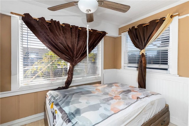 bedroom with a wainscoted wall, multiple windows, and a ceiling fan