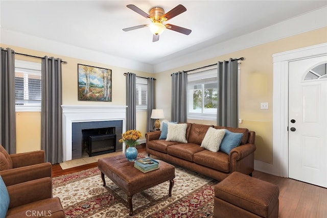 living room featuring a fireplace with flush hearth, wood finished floors, baseboards, and ceiling fan