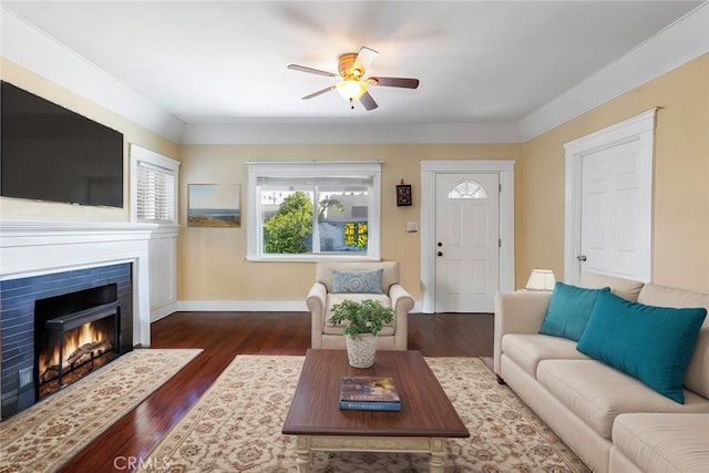 living area featuring a lit fireplace, dark wood finished floors, baseboards, and a ceiling fan