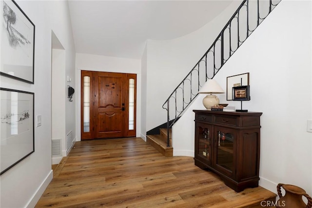 foyer entrance featuring visible vents, baseboards, wood finished floors, and stairs