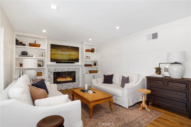 living area with visible vents, built in features, wood finished floors, a fireplace, and a decorative wall