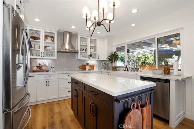 kitchen with light wood-style flooring, wall chimney exhaust hood, appliances with stainless steel finishes, and a sink