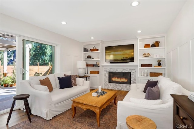 living area featuring a fireplace, a decorative wall, built in features, and wood finished floors