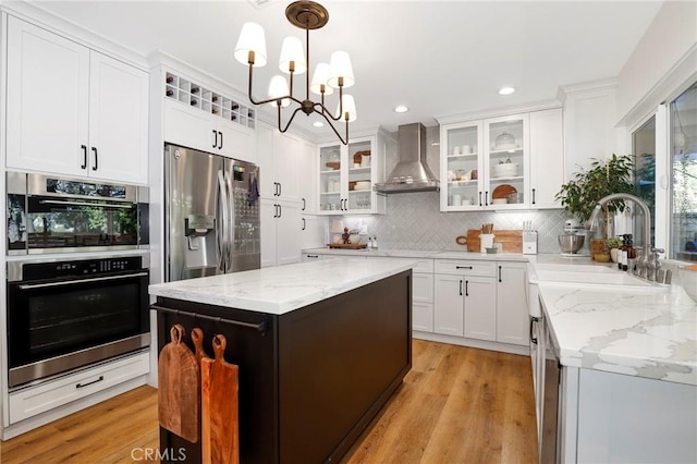 kitchen with decorative backsplash, appliances with stainless steel finishes, white cabinetry, wall chimney exhaust hood, and a sink