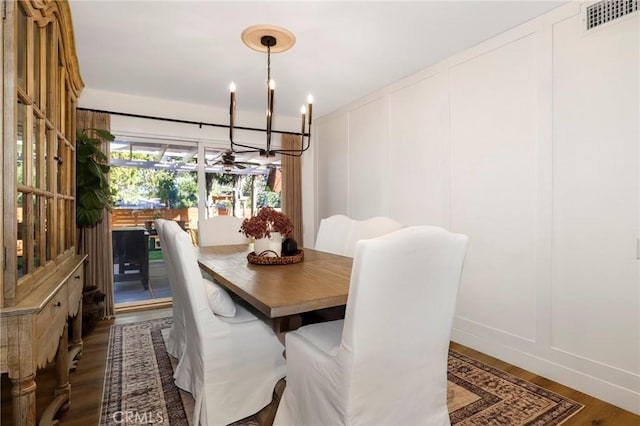 dining space with a decorative wall, a notable chandelier, visible vents, and dark wood-style flooring