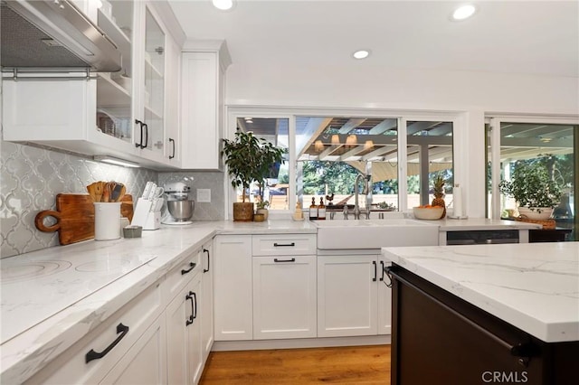 kitchen with ventilation hood, light stone countertops, white electric stovetop, white cabinetry, and a sink