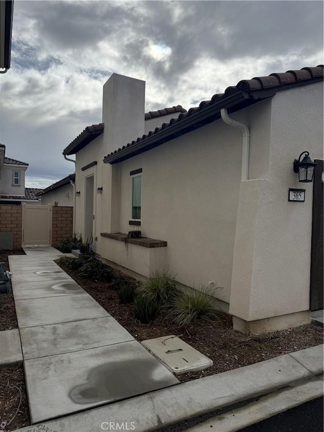 view of property exterior featuring stucco siding, a tile roof, and a gate