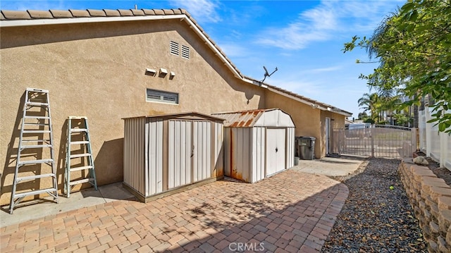 rear view of house with stucco siding, an outbuilding, a gate, fence, and a shed