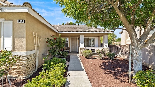 property entrance featuring a tile roof, covered porch, stone siding, and stucco siding