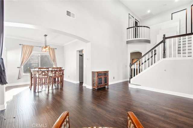 living room featuring visible vents, wood finished floors, arched walkways, baseboards, and a towering ceiling