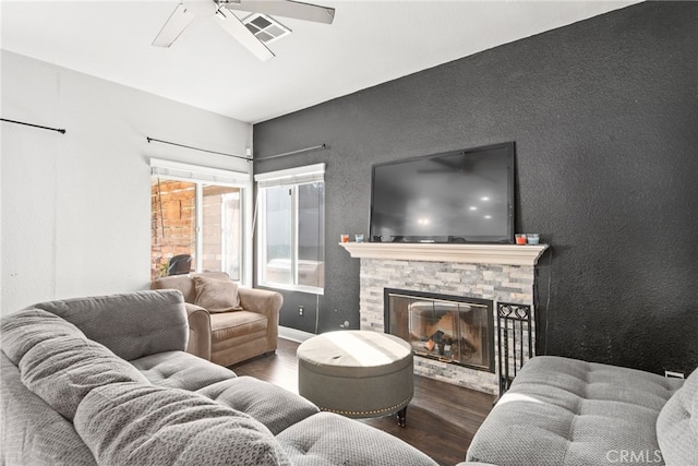 living area featuring a stone fireplace, wood finished floors, visible vents, and ceiling fan