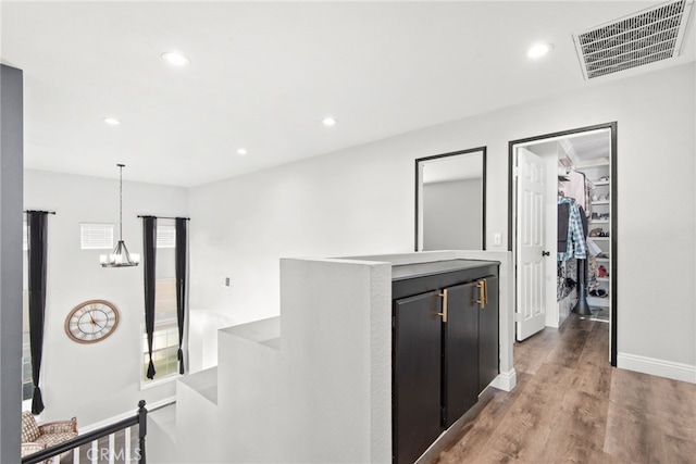 hallway with visible vents, an upstairs landing, an inviting chandelier, and wood finished floors