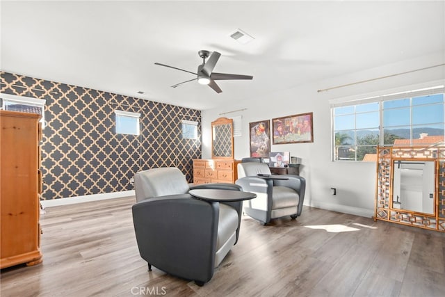 living area featuring light wood-type flooring, visible vents, baseboards, and wallpapered walls