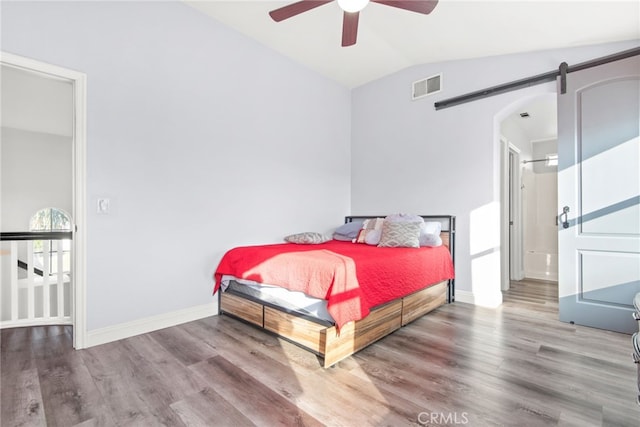 bedroom with visible vents, wood finished floors, a barn door, baseboards, and vaulted ceiling