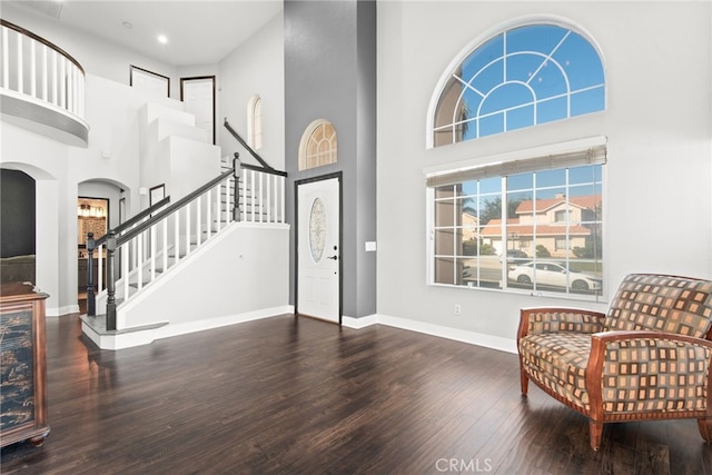 foyer entrance with wood finished floors, baseboards, arched walkways, stairs, and a towering ceiling