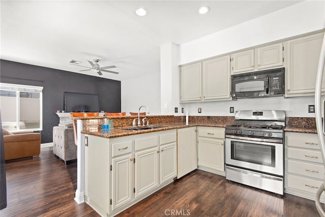 kitchen with a sink, open floor plan, a peninsula, black microwave, and stainless steel gas range